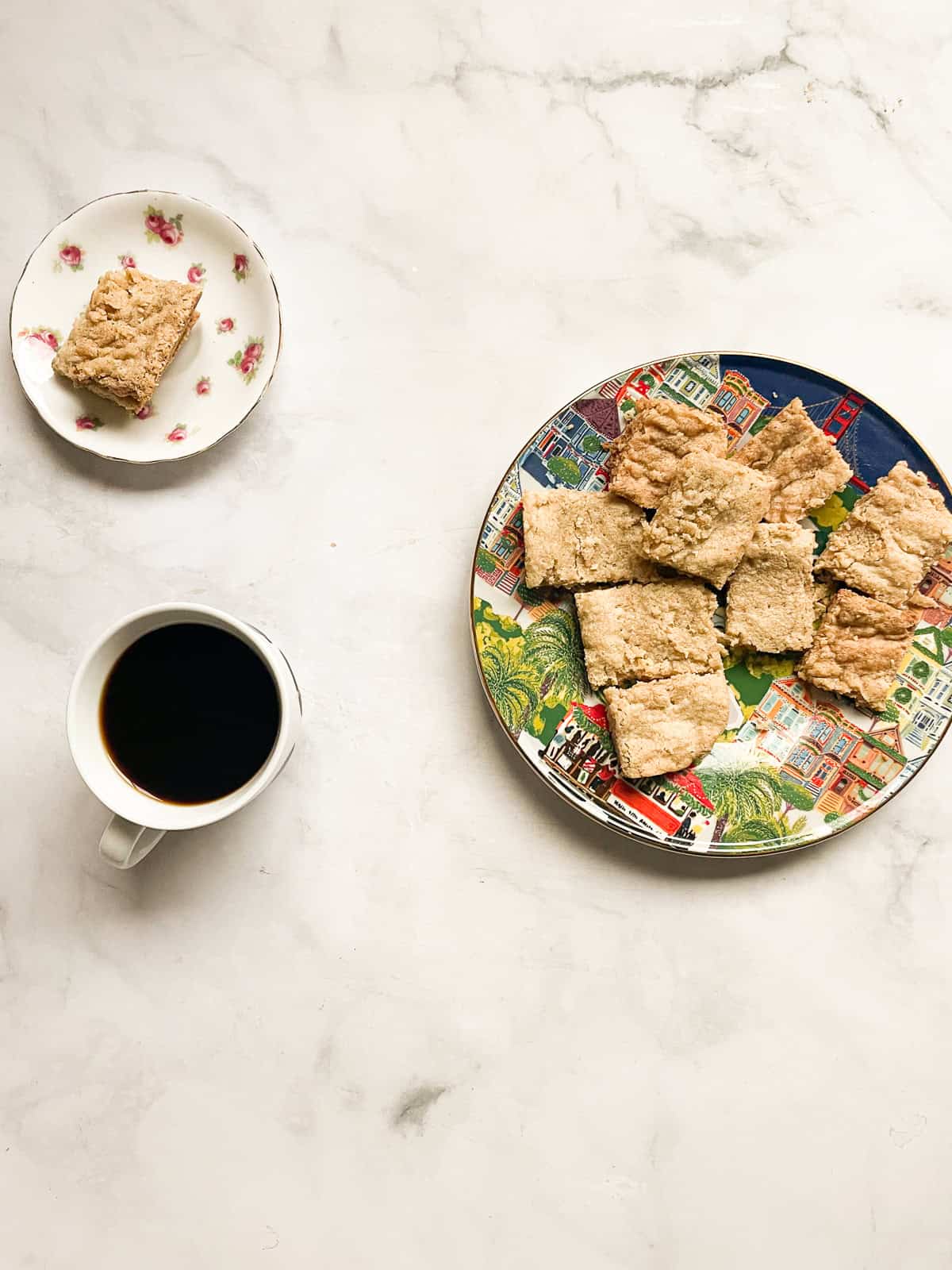 A cup of coffee next to a square of shortbread on a plate with a plate of maple shortbread.