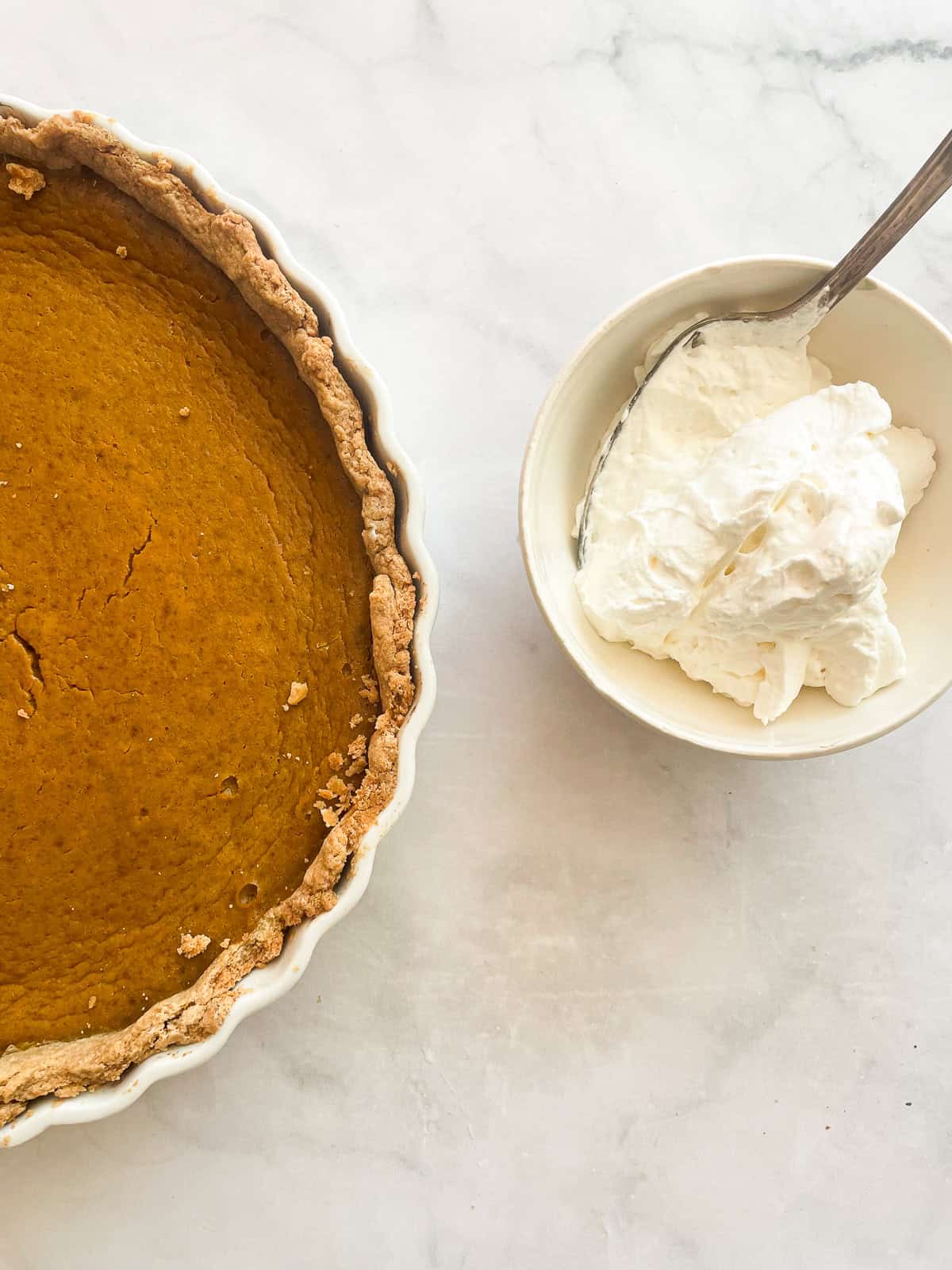 A pumpkin pie with a bowl of whipped cream.