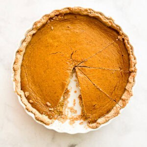 A pumpkin pie with whipped cream with a slice removed.