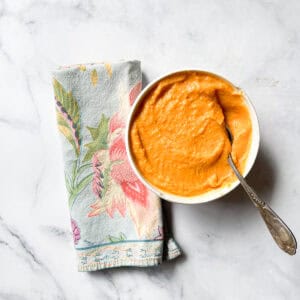 A napkin lies next to a bowl of sweet potato and coconut soup with a spoon.