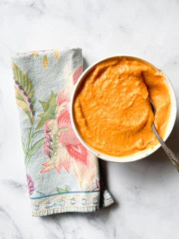 A napkin lies next to a bowl of sweet potato and coconut soup with a spoon.