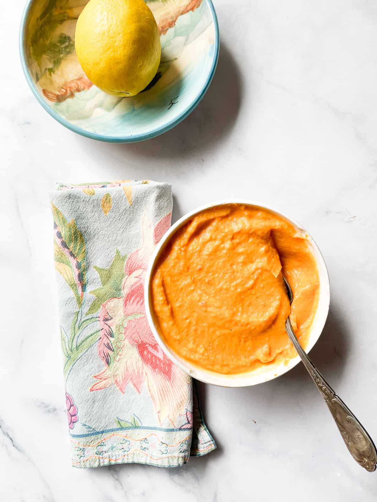 A lemon in a bowl next to a bowl of sweet potato and coconut soup.