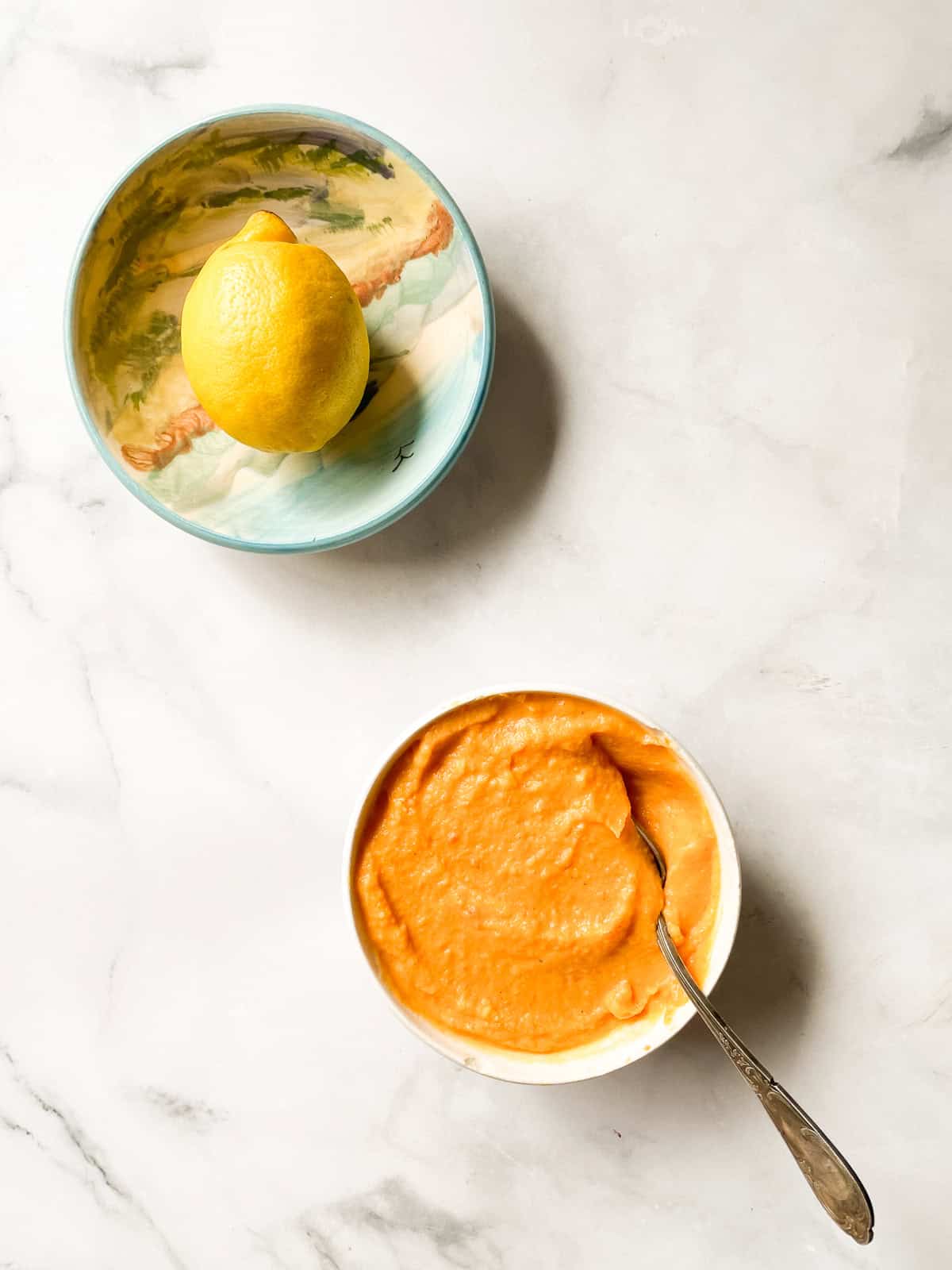 A bowl of sweet potato and coconut soup with a spoon and a lemon in a bowl.