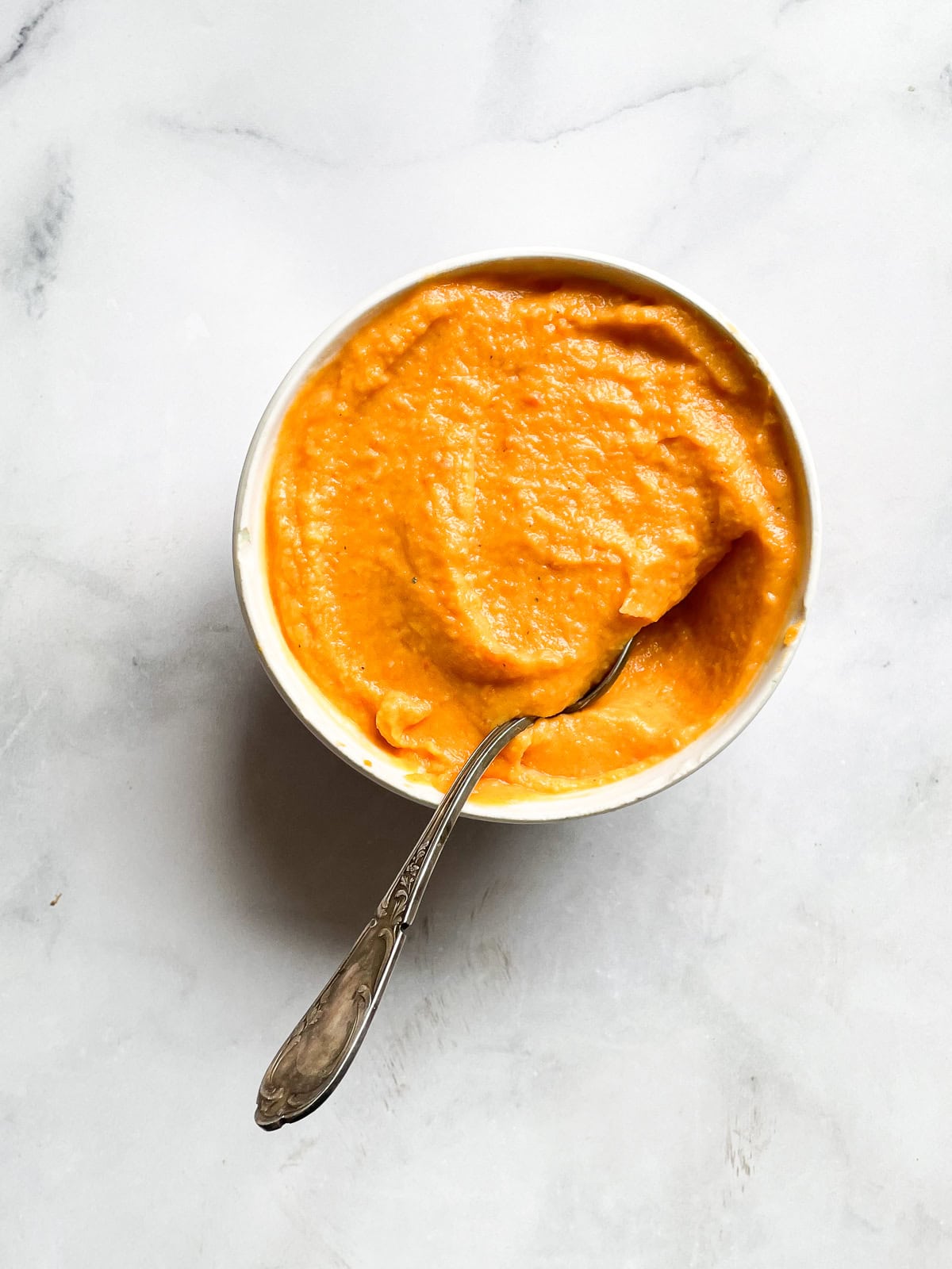 A bowl of sweet potato and coconut soup with a spoon