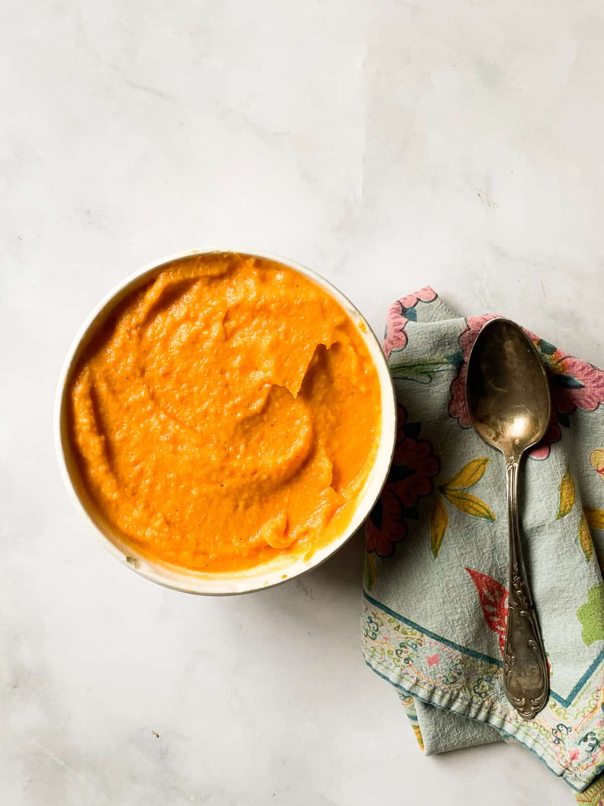 A bowl of sweet potato and coconut soup on a counter with a napkin and spoon.