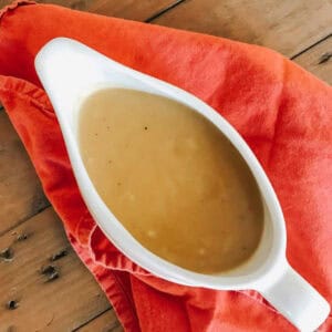 A gravy tureen with vegetarian gravy on top of a red napkin.