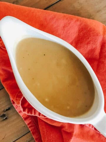 A gravy tureen with vegetarian gravy on top of a red napkin.