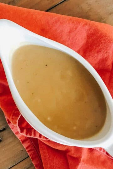 A gravy tureen with vegetarian gravy on top of a red napkin.