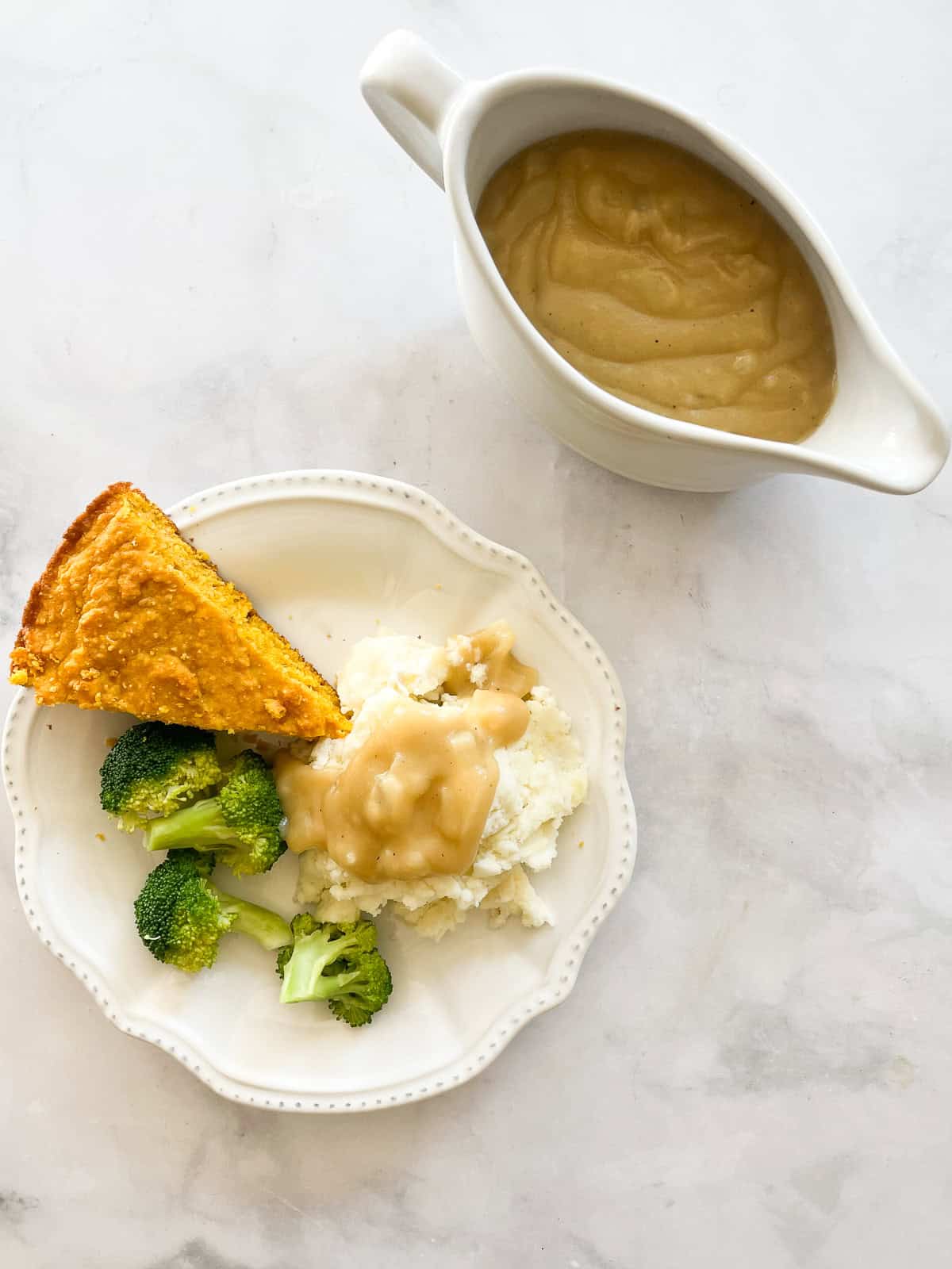 A plate of cornbread, mashed potatoes, broccoli and vegetarian gravy with a tureen of gravy.