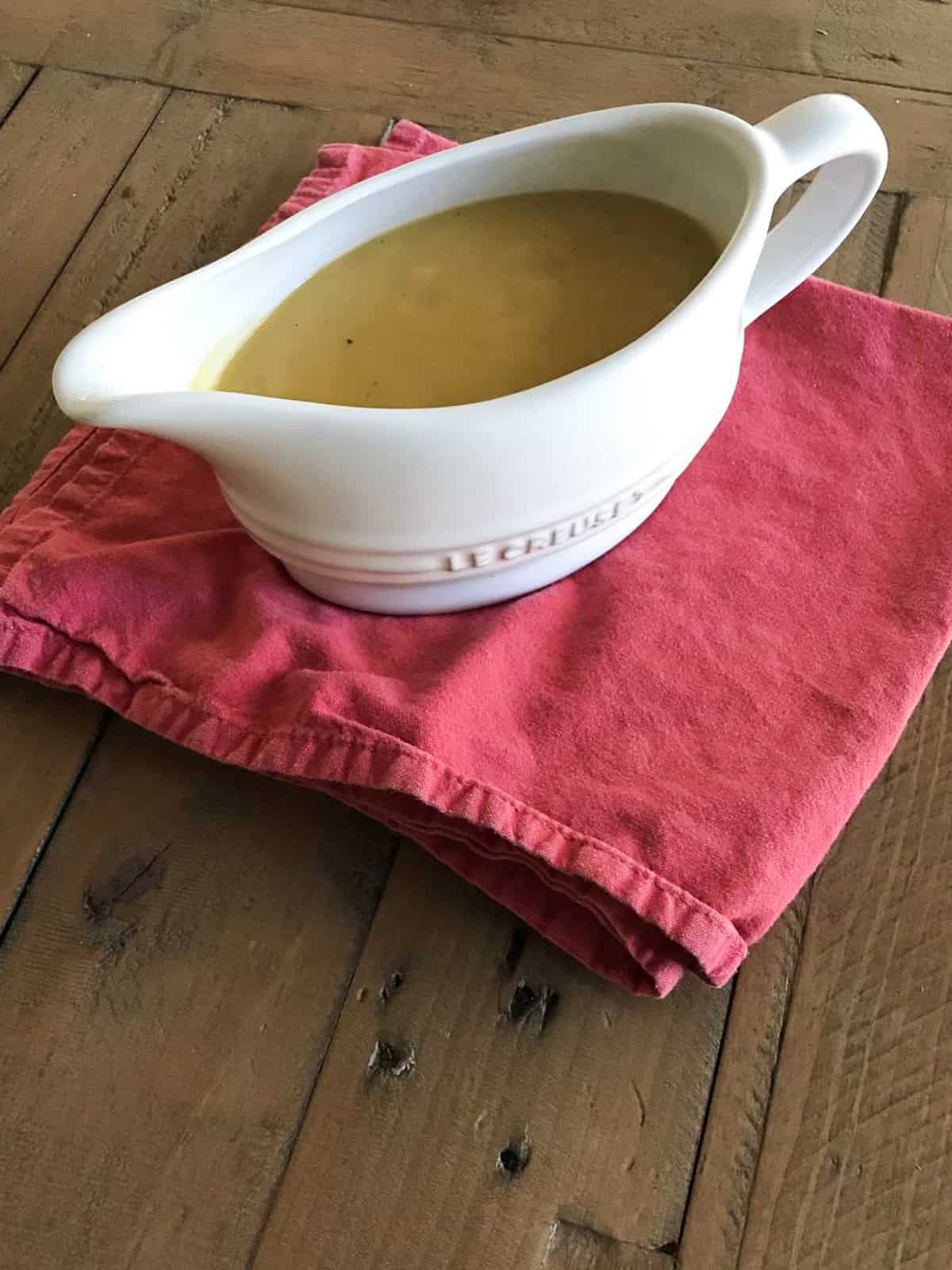 A pitcher of vegetarian gravy on a red napkin on a wooden table.