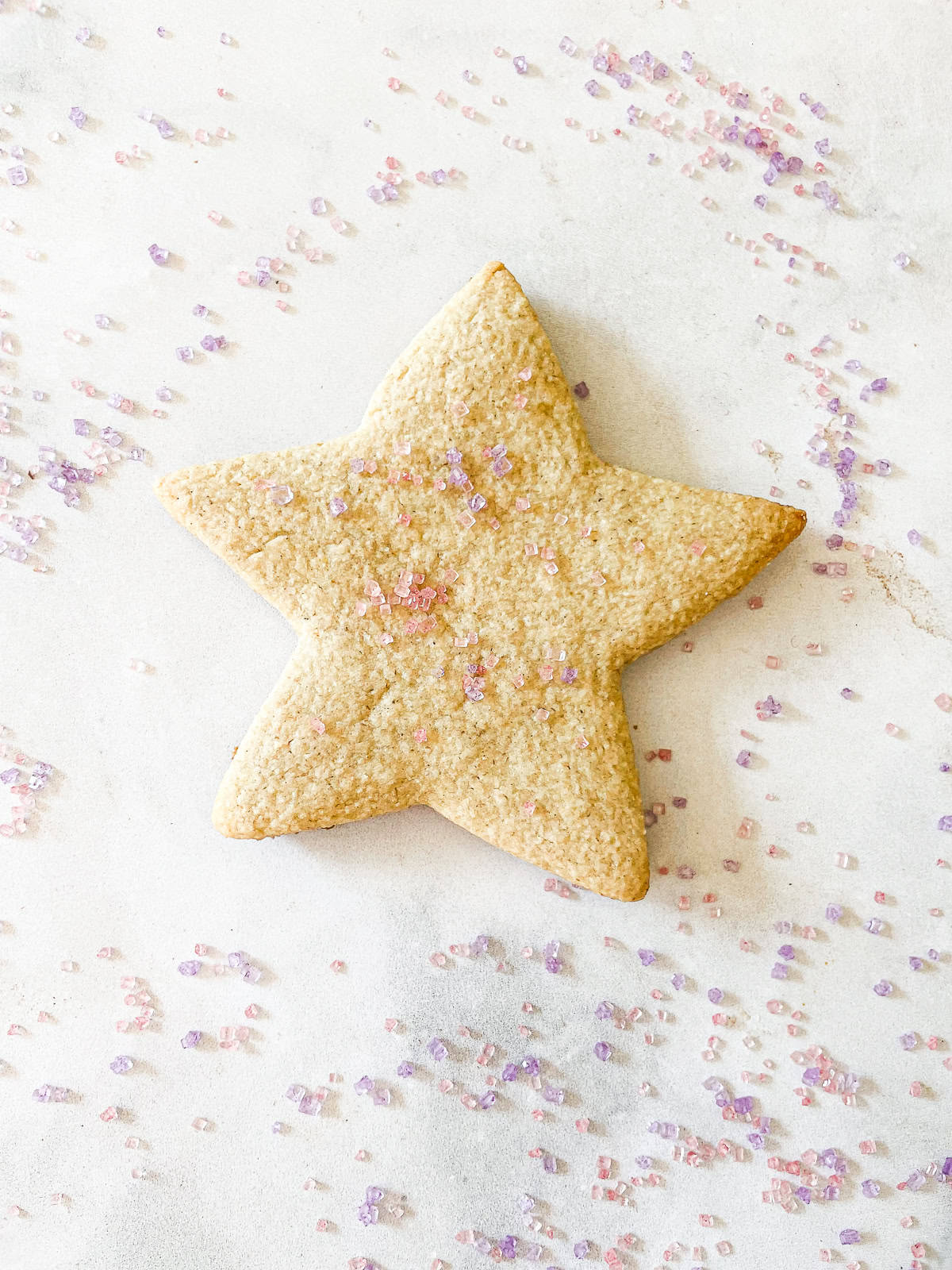 Sprinkles surround a gluten free sugar cookie.