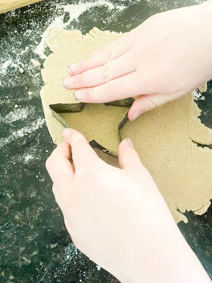 A kid's hands press out sugar cookies.