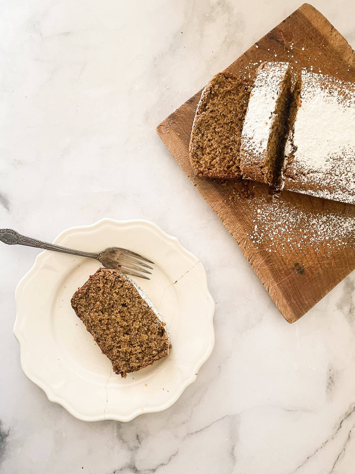 A slice of gingerbread on a plate with a fork and the loaf next to it.