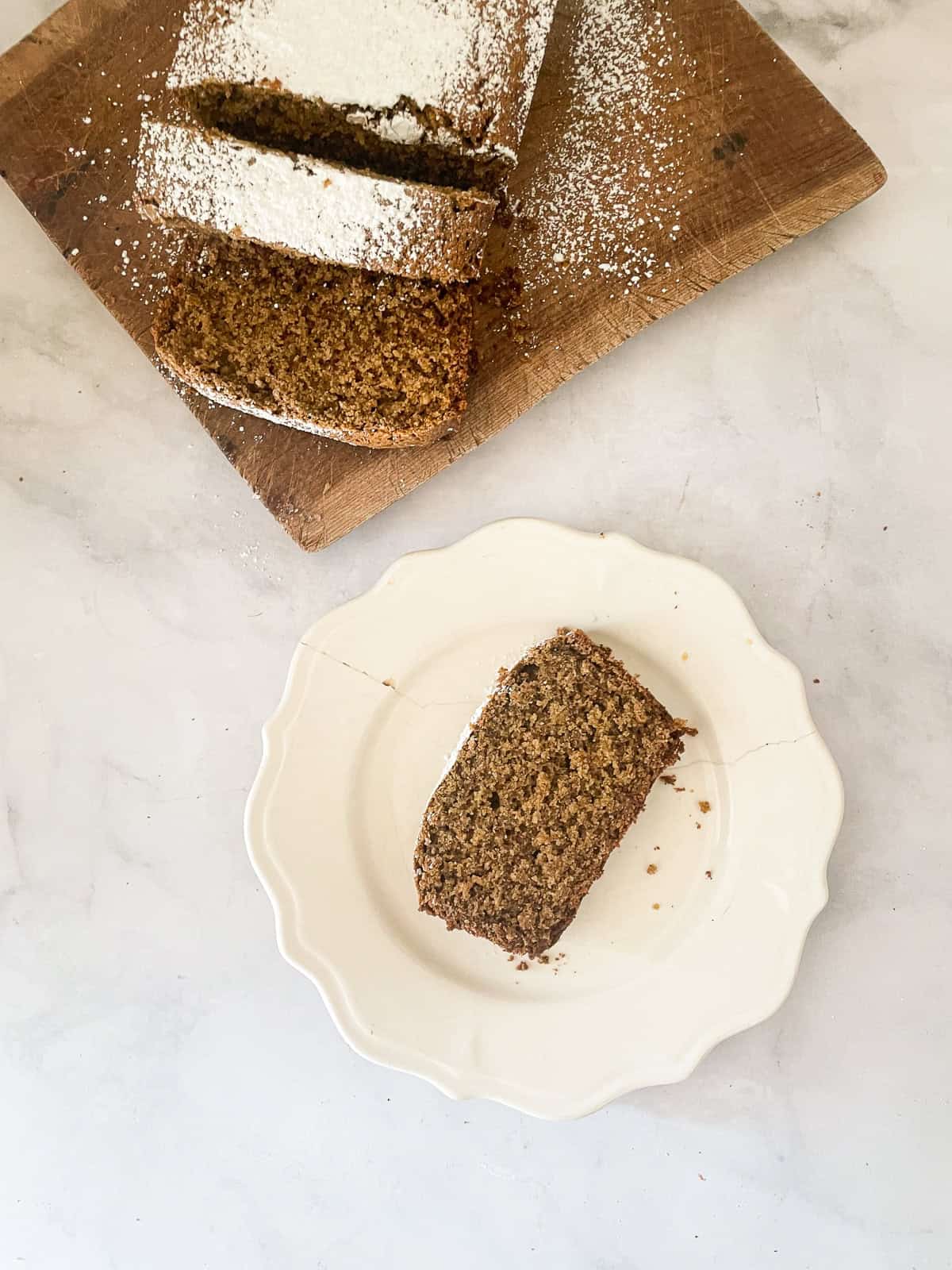 A slice of gingerbread loaf on a plate with the loaf on a board.