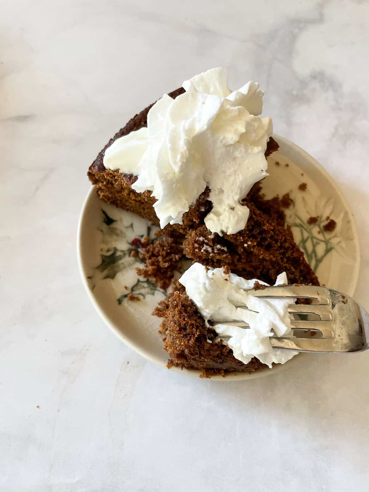 Whipped cream on top of a slice of gluten-free gingerbread.