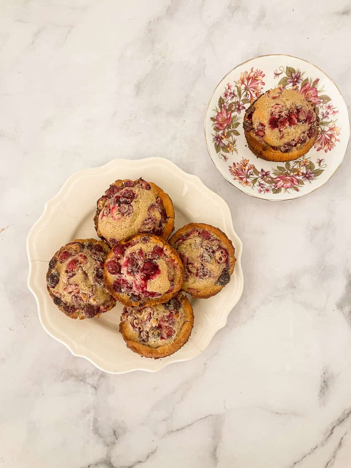 Four orange cranberry muffins on a plate and a muffin on a plate.