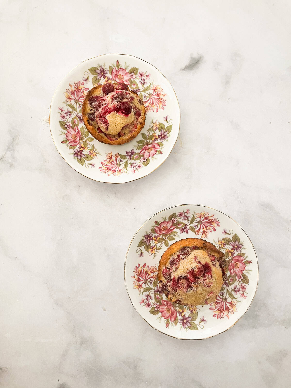 Two orange cranberry muffins on plates.