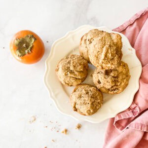 Gluten free persimmon muffins on a plate with a persimmon next to them.