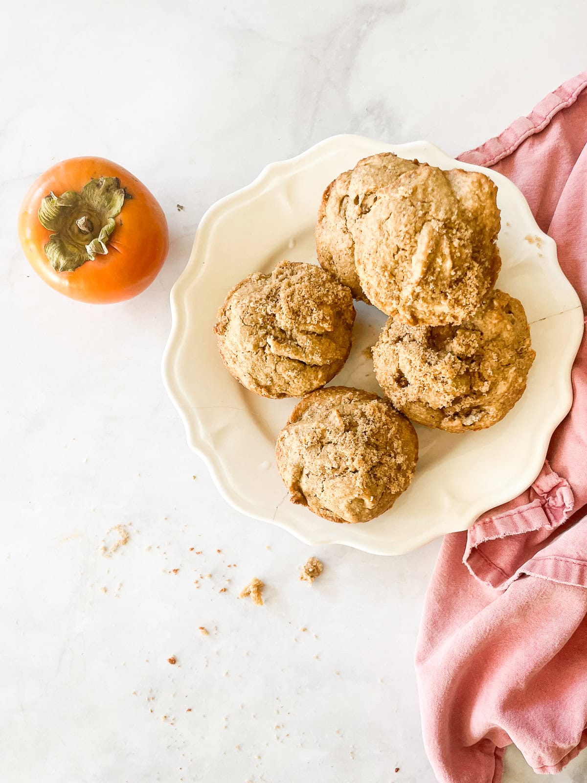 Gluten free persimmon muffins on a plate with a persimmon next to them.