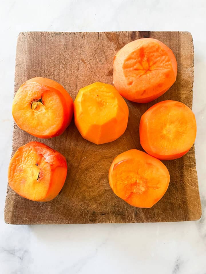 Persimmons on a cutting board with tops removed.