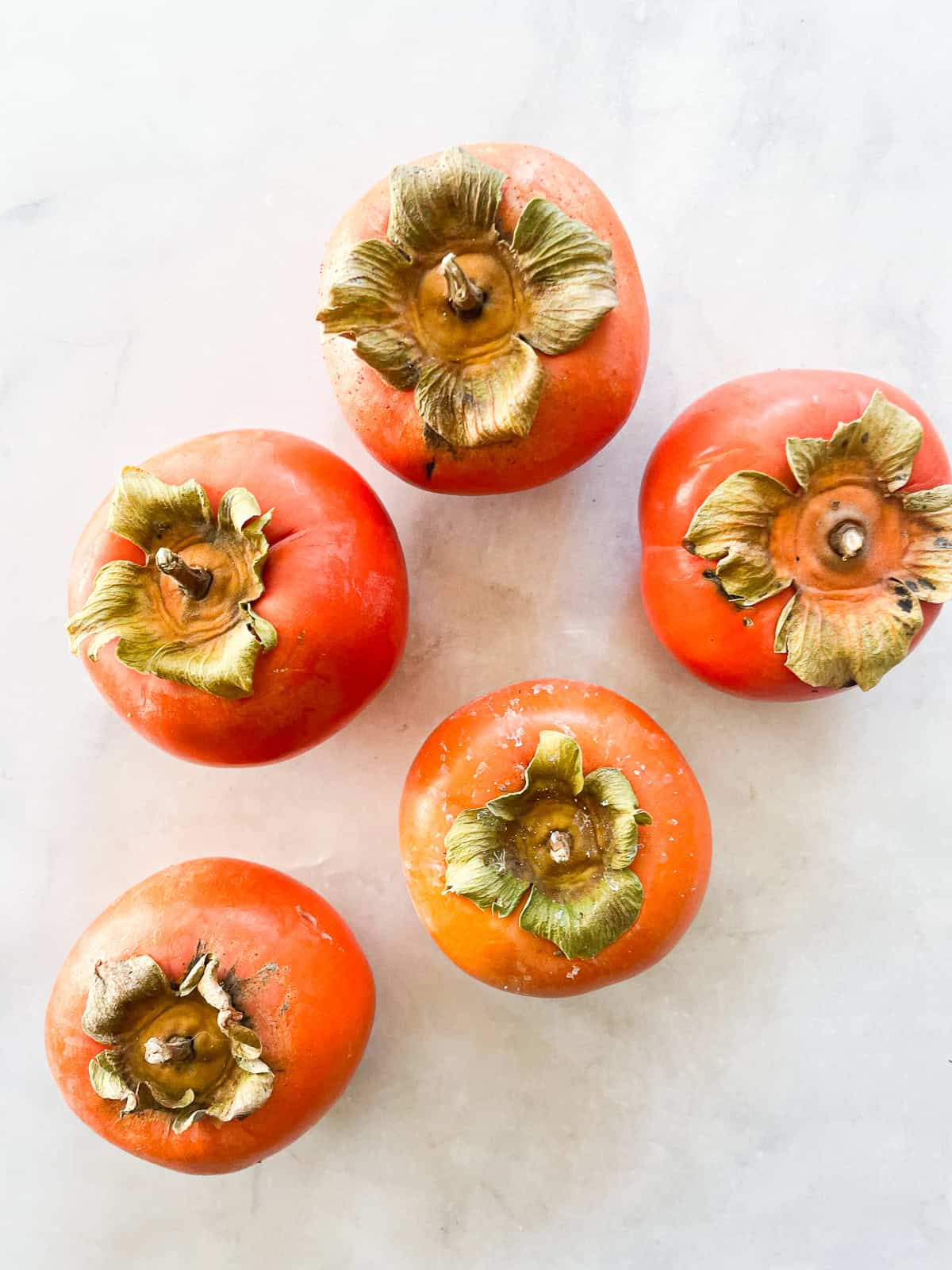 Five fuyu persimmons on a counter.