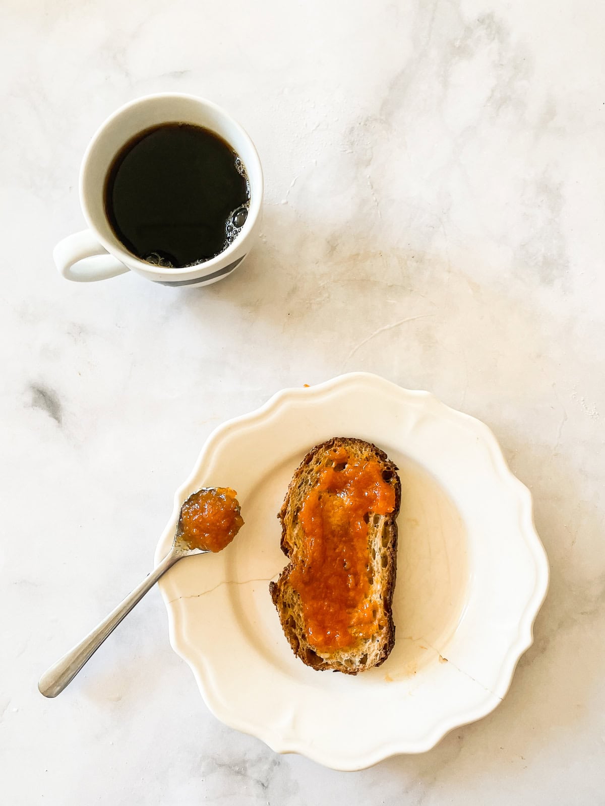 A cup of coffee and a plate with toast and persimmon jam.