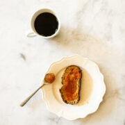 A cup of coffee and a plate with toast and persimmon jam.