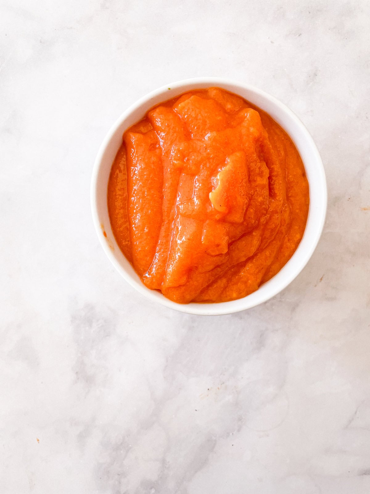 A white bowl of orange persimmon puree.