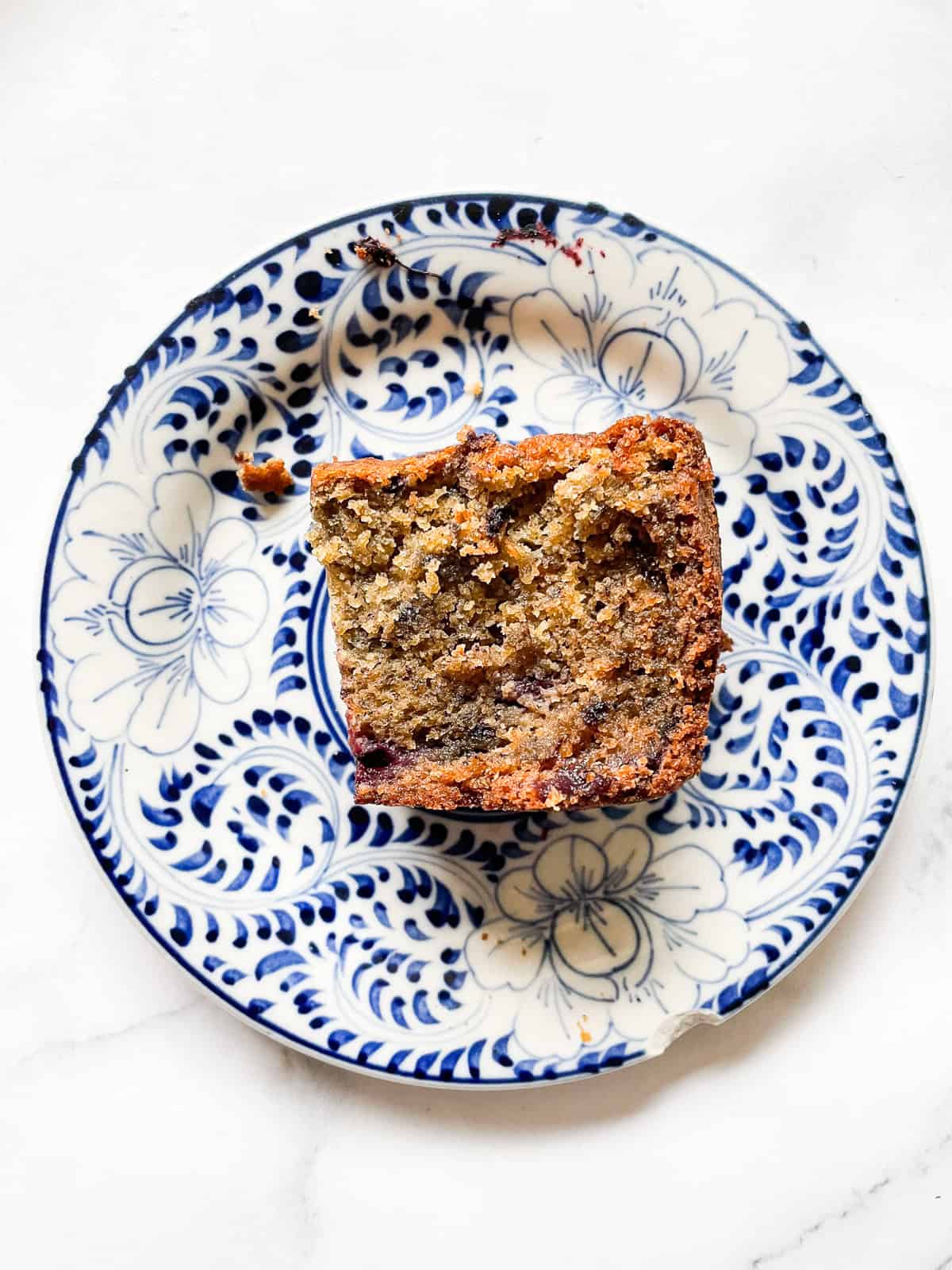 A small slice of banana blackberry bread on a blue and white plate.