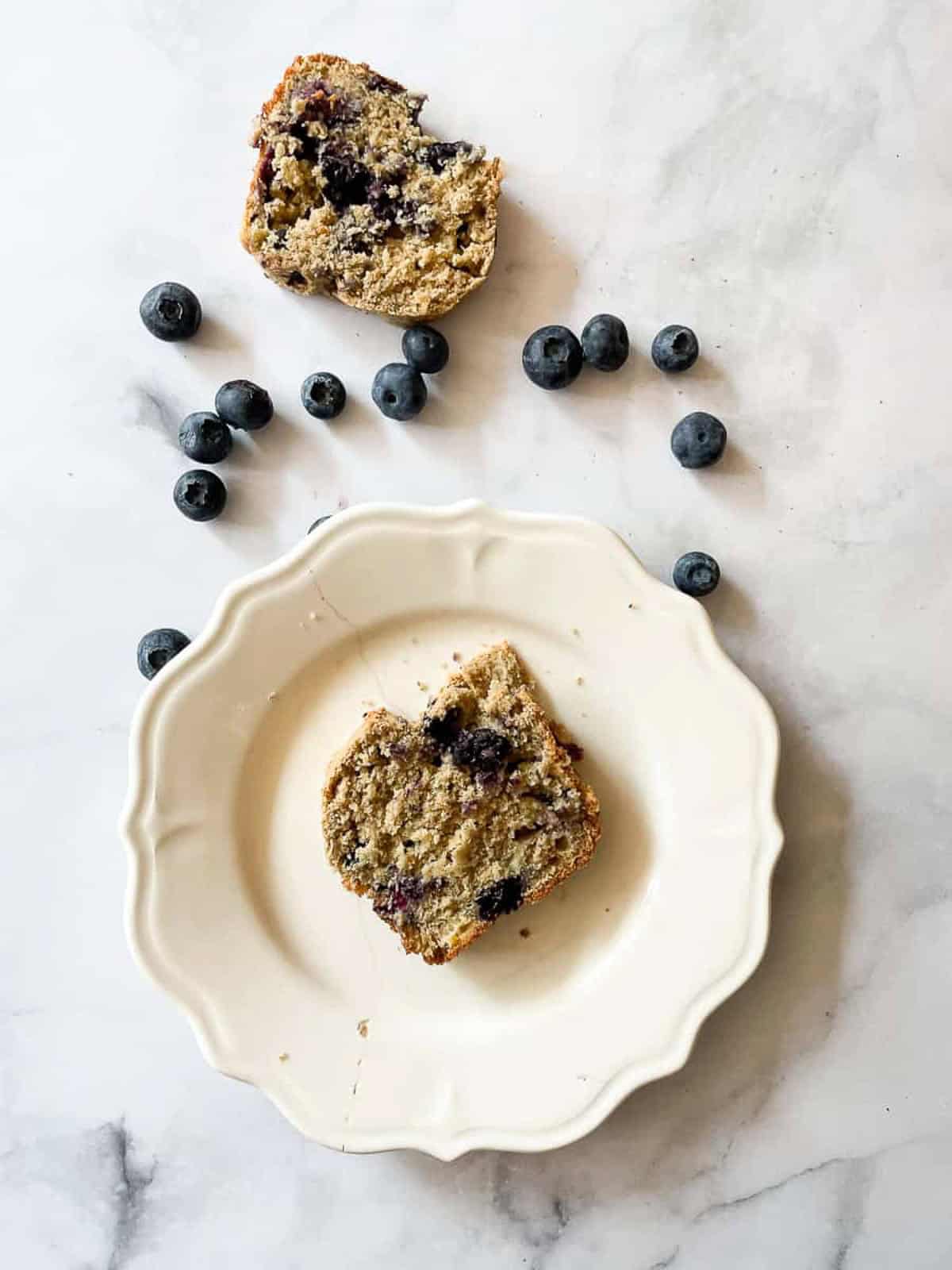 A piece of blueberry banana bread on a plate surrounded by blueberries.