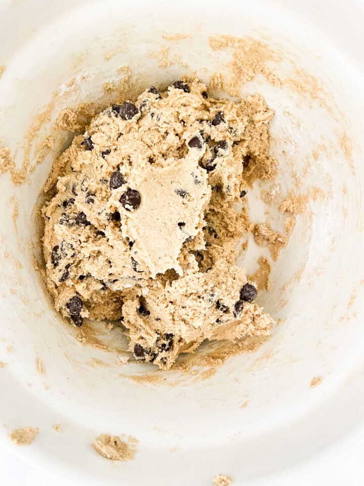 Chocolate chips are added to cookie dough in a bowl.