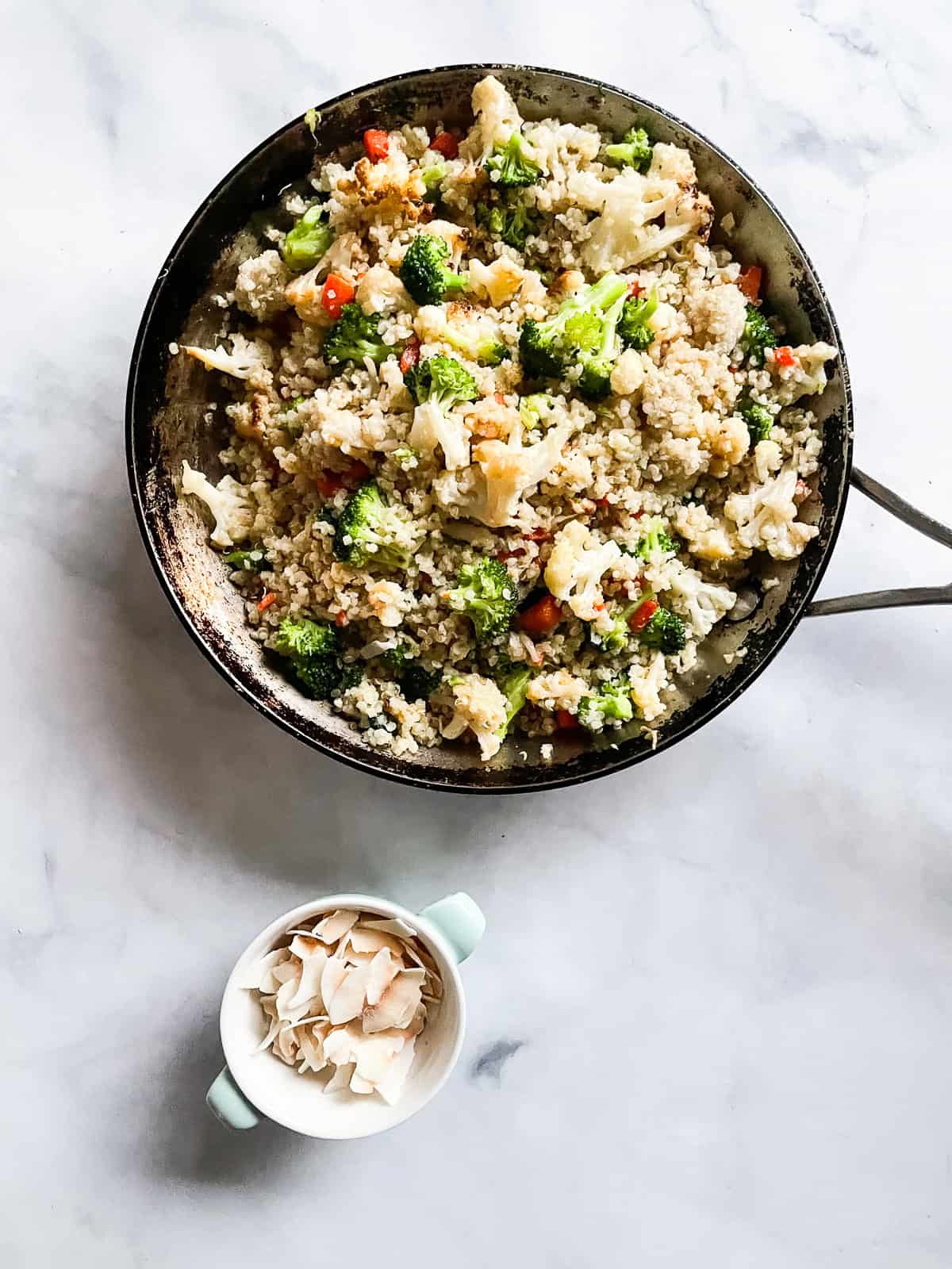 A dish of toasted coconut next to a skillet of coconut quinoa.