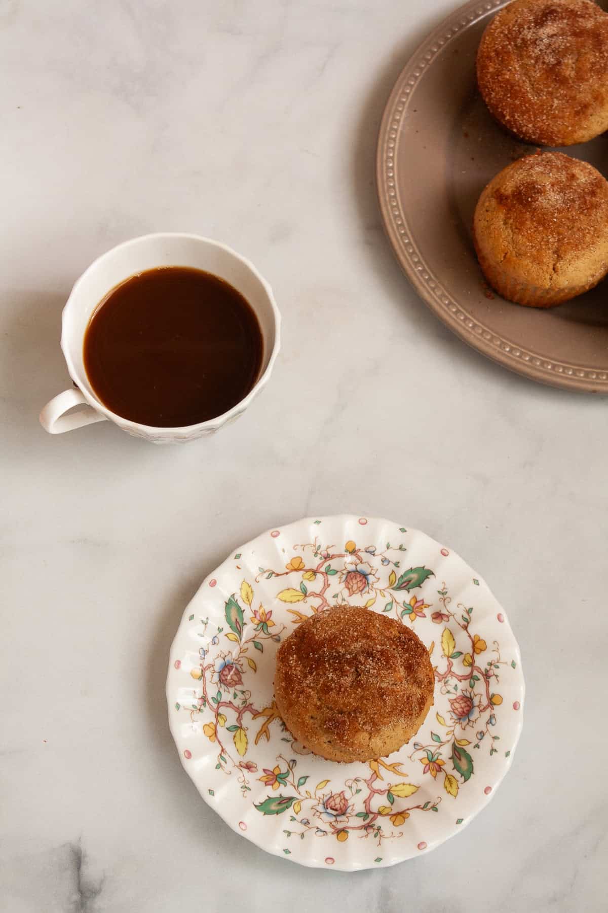 A cup of tea, a gluten free donut muffin on a plate, and muffins on plate.