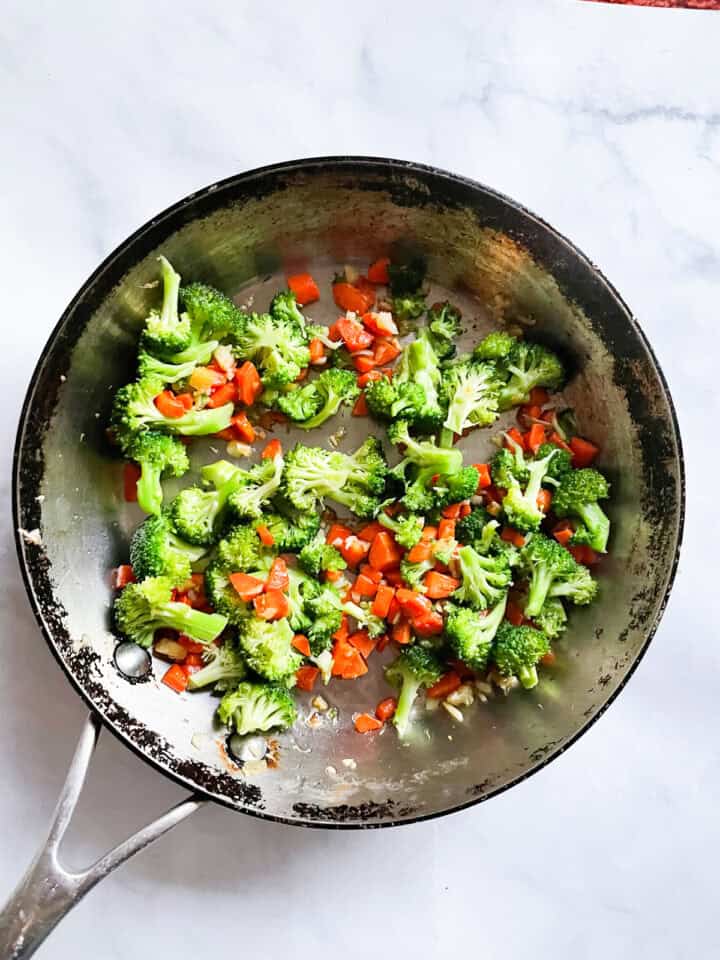 Cauliflower and veggies sautee in a skillet.