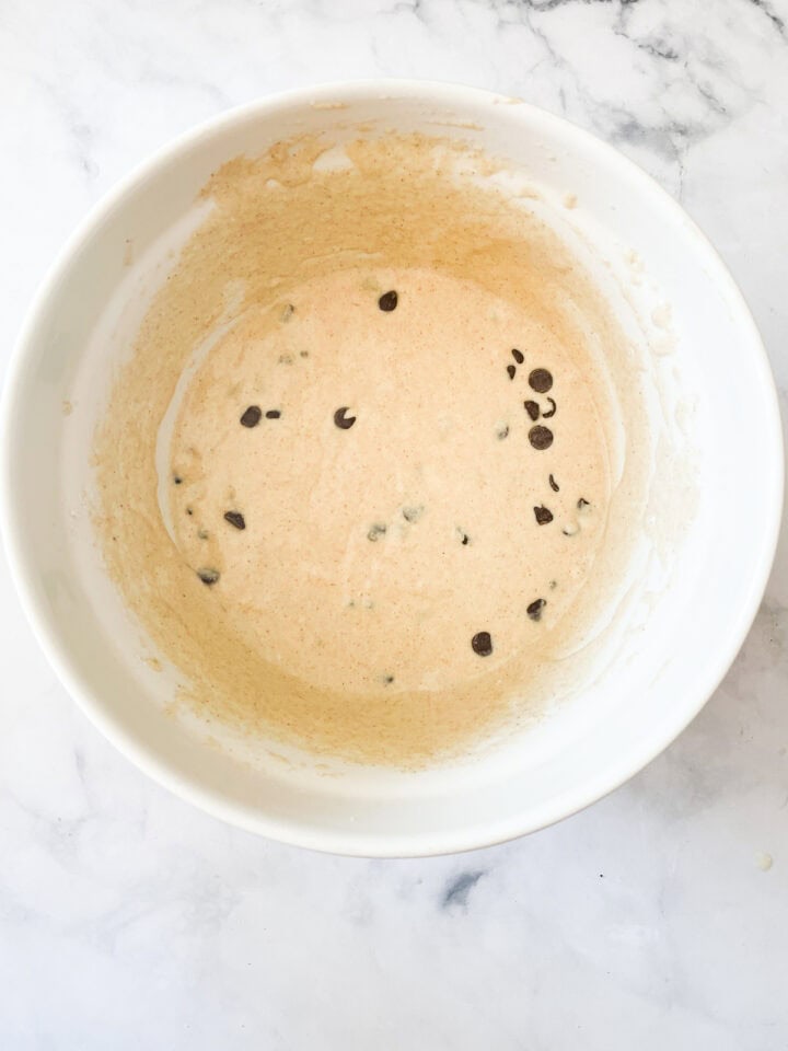 Chocolate chips are added to muffin batter in a bowl.