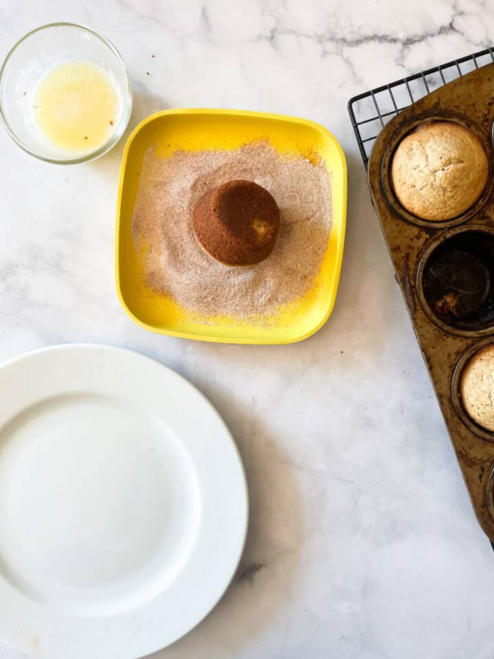 A donut muffin is dipped in cinnamon sugar.