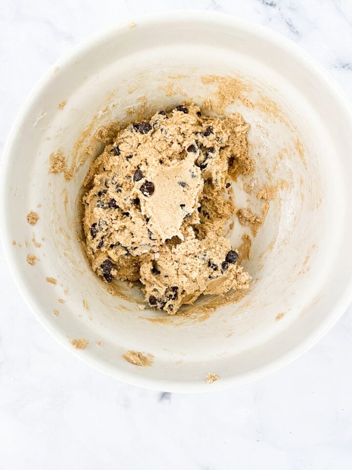 Chocolate chips are added to cookie dough in a bowl.