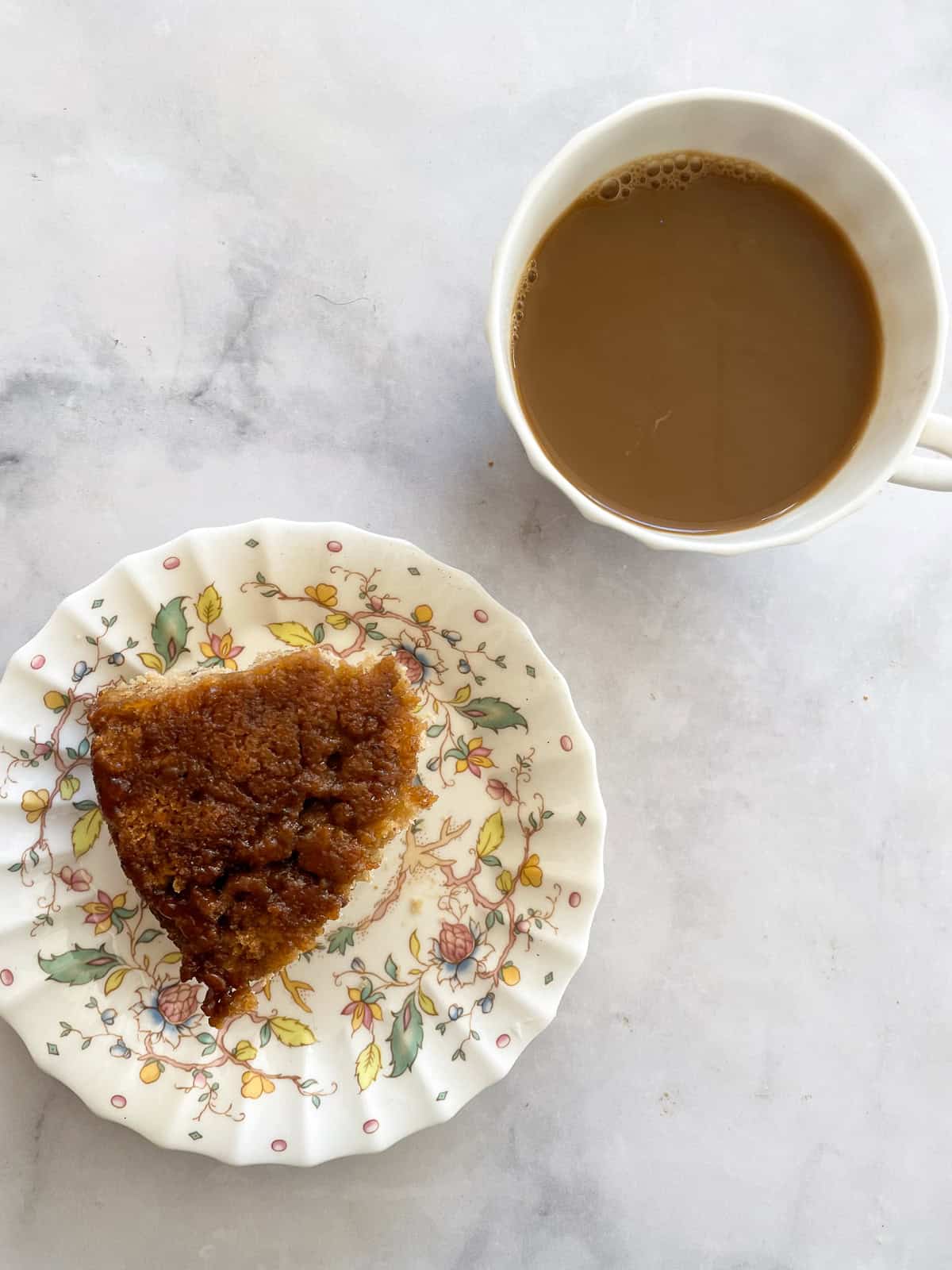 An oat flour cinnamon roll with maple glaze on a plate with a cup of coffee.