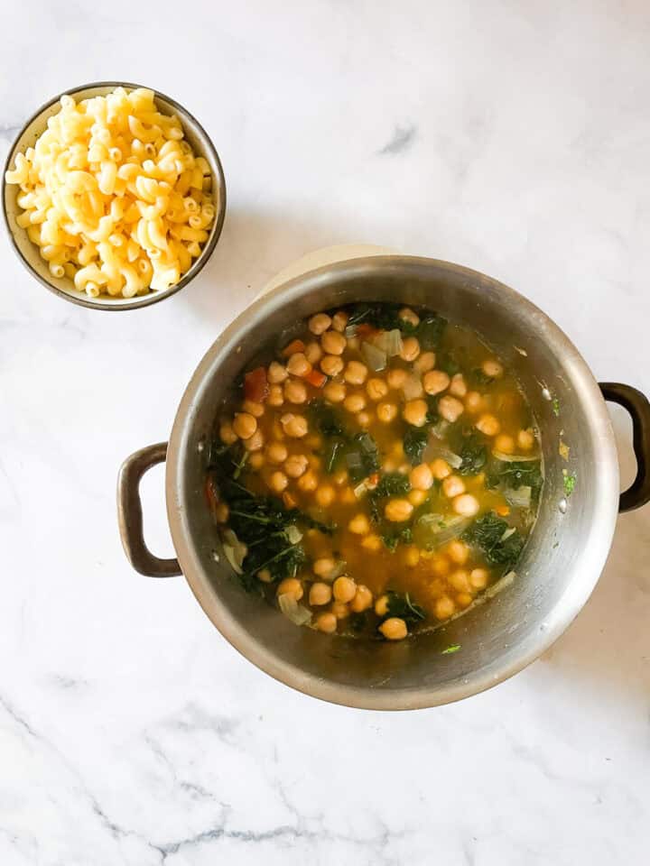 A bowl of cooked pasta next to a pot of soup.