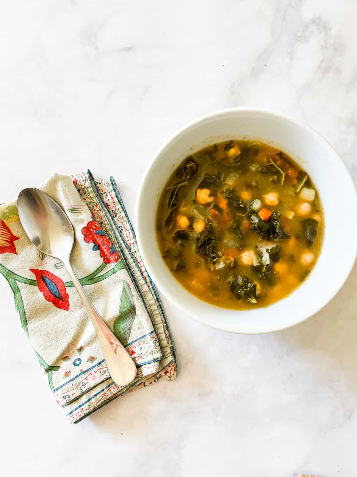 A spoon on a napkin next to a bowl of vegetarian minestrone soup.