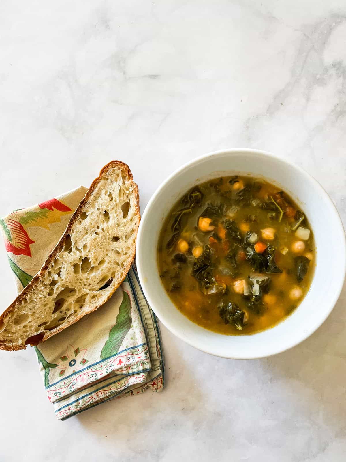 A slice of bread on a napkin next to a bowl of soup.