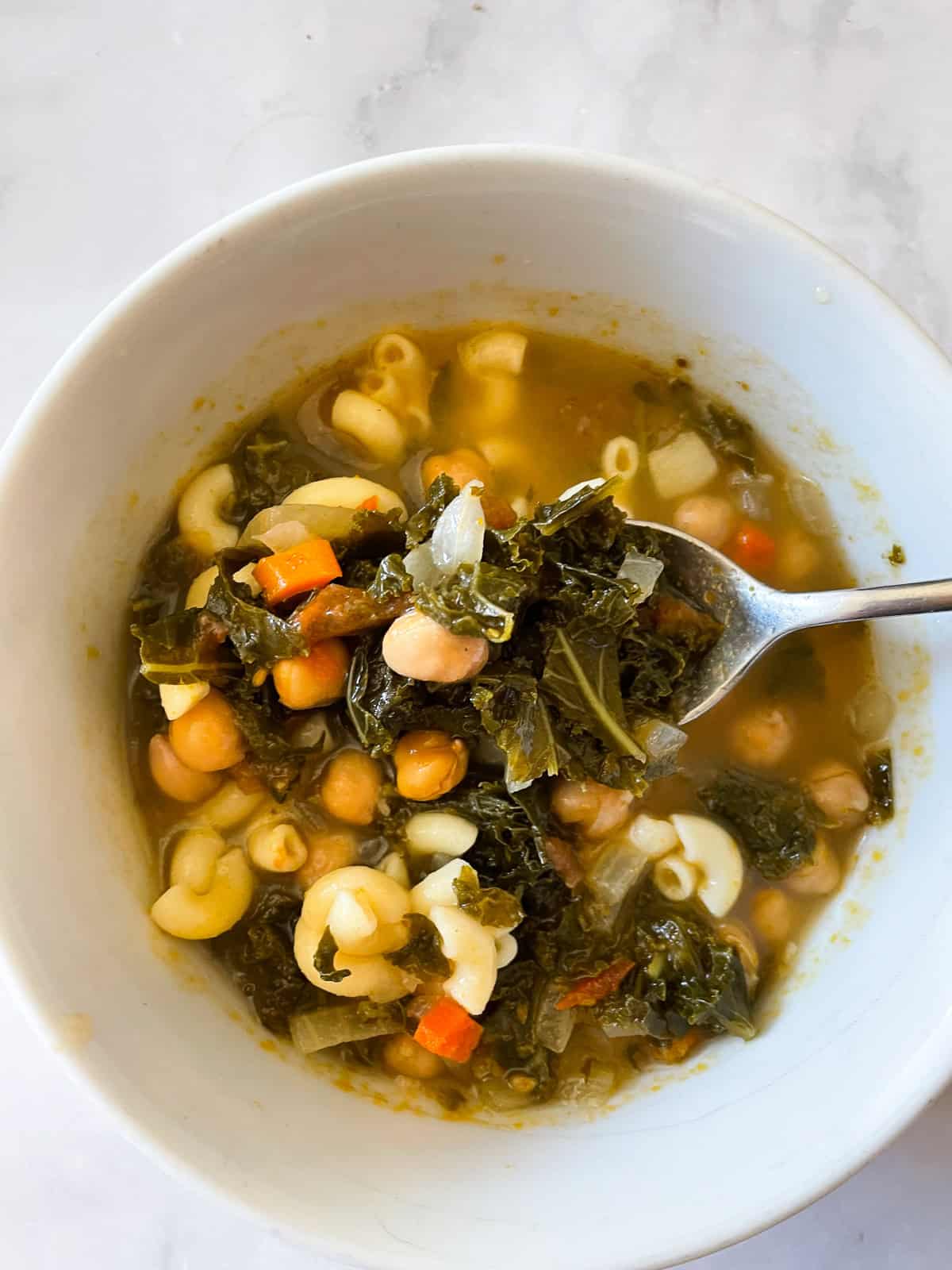 A spoonful of minestrone soup above a bowl of soup.