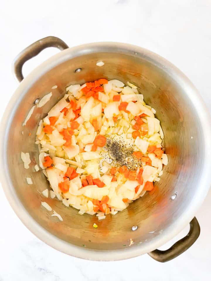 Salt and pepper season onions, garlic, and carrots in a pot.