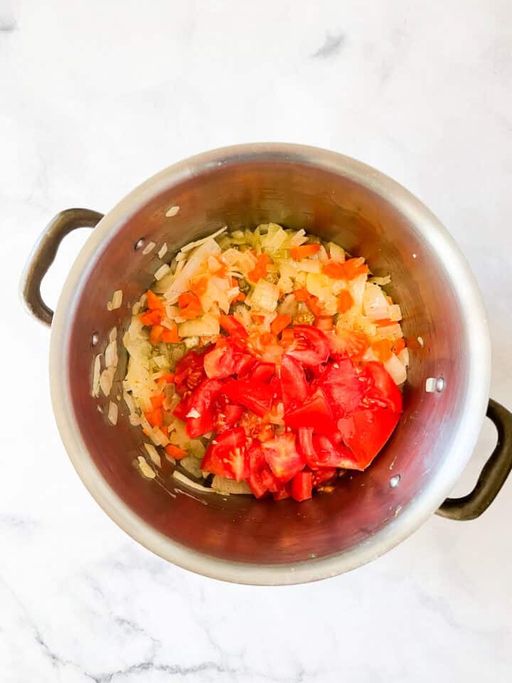 Tomatoes are added to a soup base in a pot.