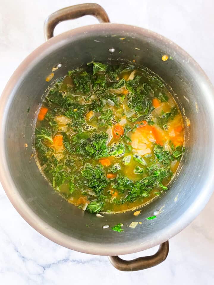 Kale is added to a pot of minestrone soup.