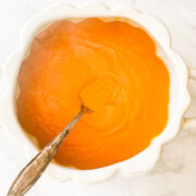 A white serving dish with butternut squash puree and a spoon.