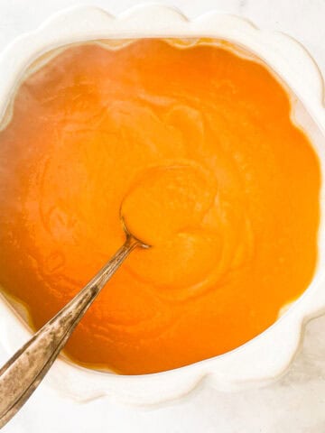 A white serving dish with butternut squash puree and a spoon.