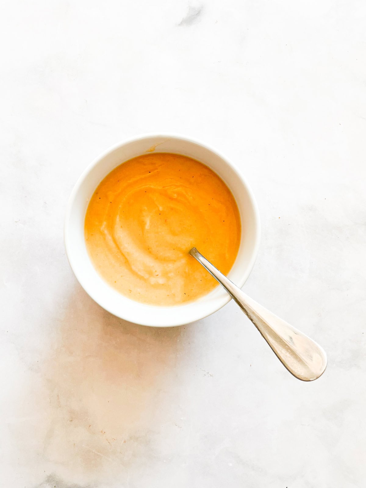 A bowl of carrot cauliflower soup with a spoon.