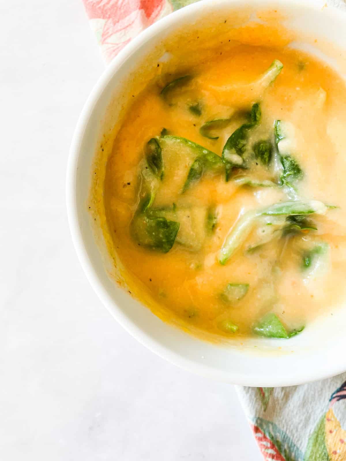 Spinach leaves in a bowl of carrot cauliflower soup.