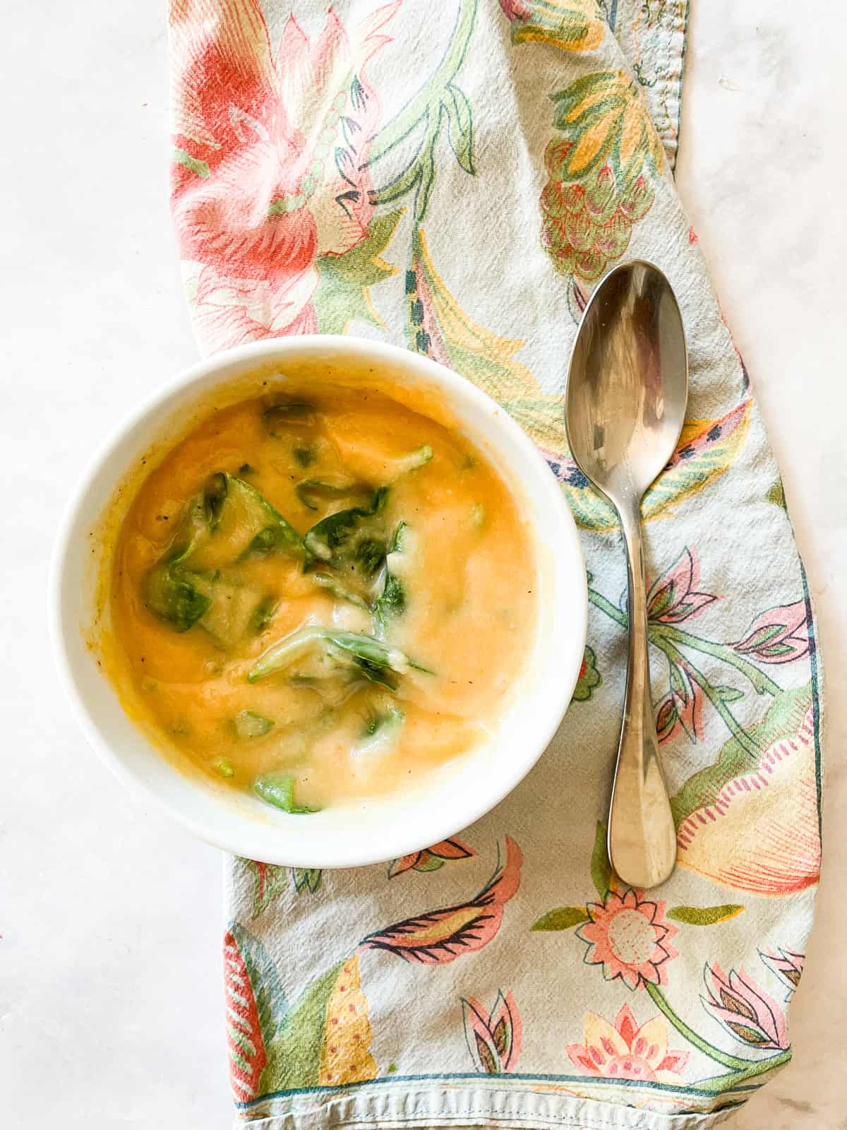 A bowl of carrot cauliflower soup with spinach on a napkin.